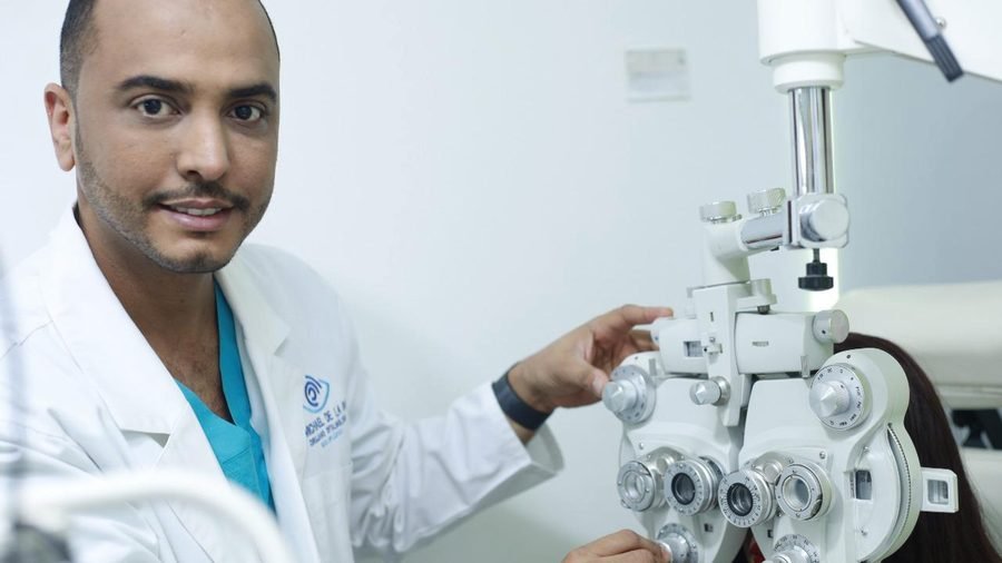 El Dr. Michael De la Rosa ajustando un foróptero durante una consulta oftalmológica.